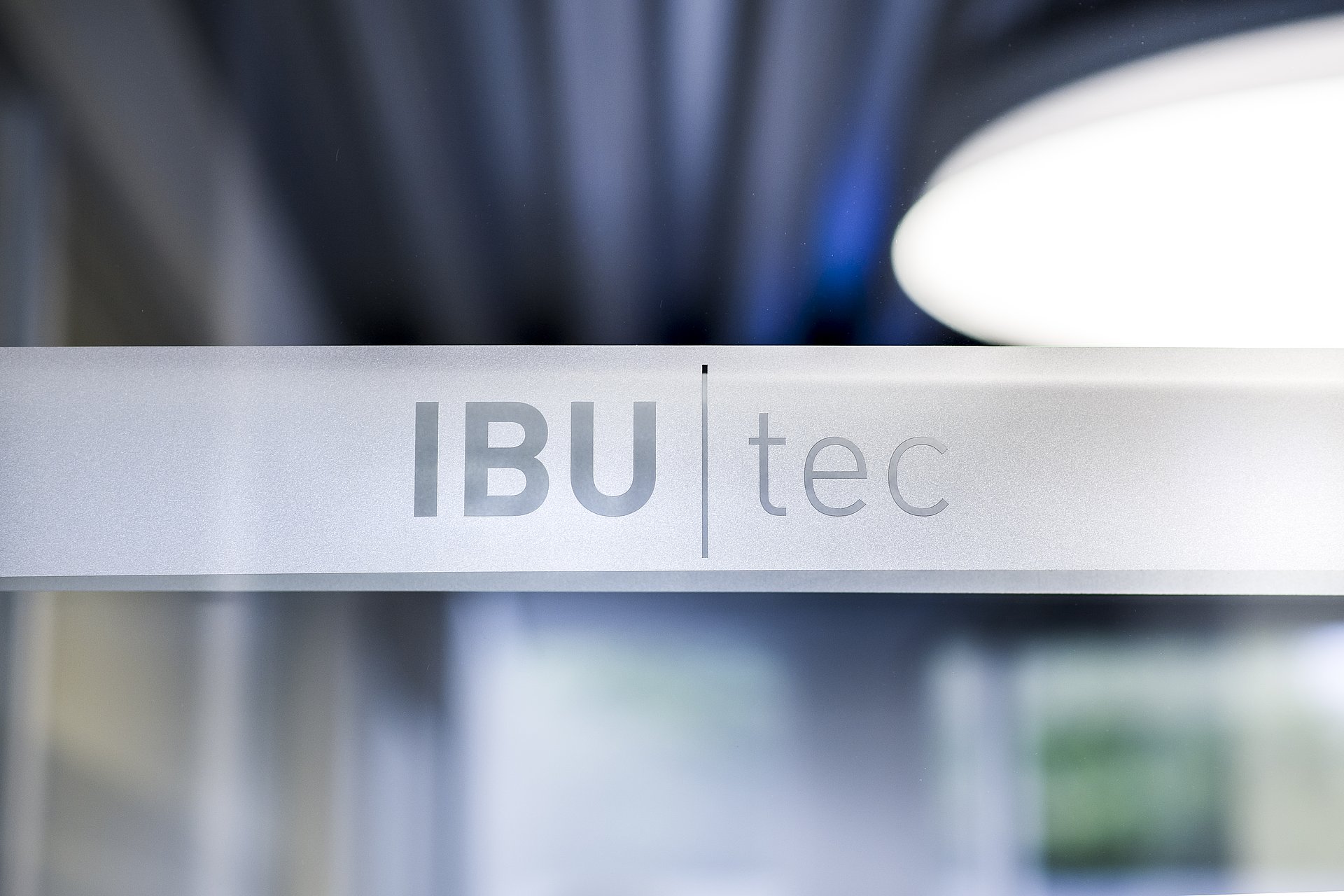 IBU-tec Logo mit künstlerischen unscharfen Lichtern im Hintergrund: blau, grau und weiß