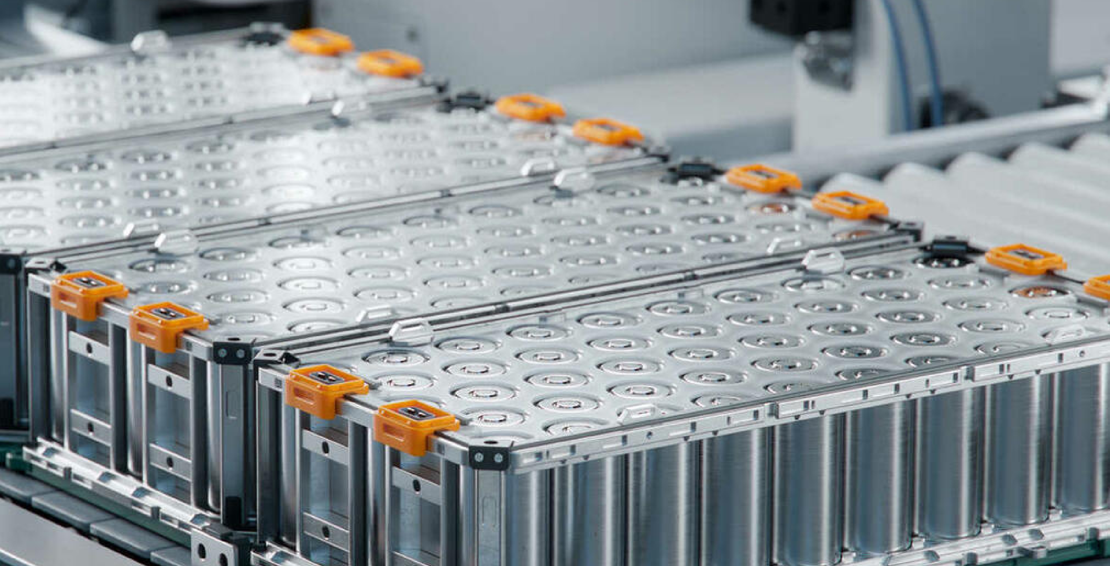 Vier Boxen mit Batteriezellen auf einem Fließband in einem hell ausgeleuchteten Produktionsbereich